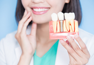 smiling woman holding up a sideview of a jaw with a dental implant inserted