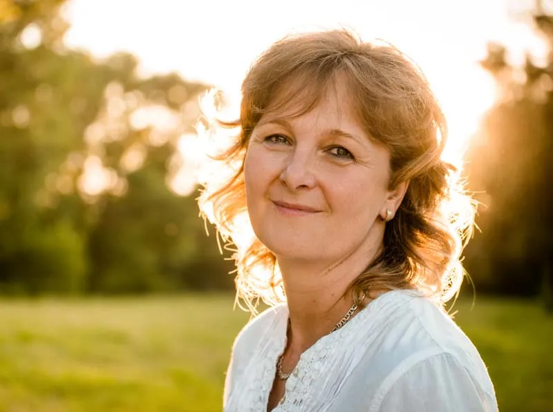 A woman smiling in an open field with the sun illuminating her hair